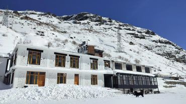Snow-covered hotel building against a mountainous backdrop under a clear blue sky.
