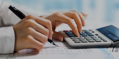 Hands using a pen and calculator to work on financial documents.