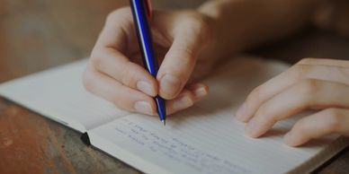 Person writing notes with a blue pen in a notebook.
