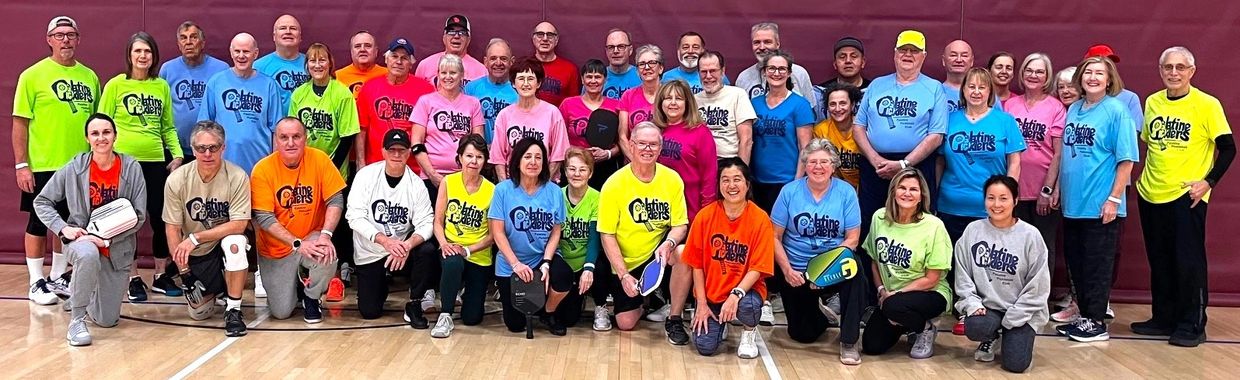 Group photo of pickleball players in colorful shirts on indoor court.