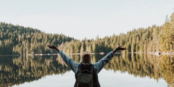 Person stretching their arms toward the sky in front of a reflective lake
