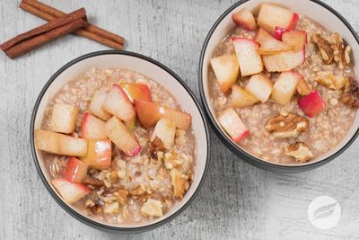 Two bowls of oatmeal topped with diced apples and walnuts, with cinnamon sticks nearby.