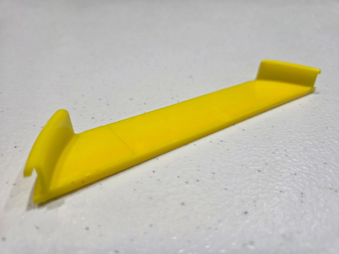 Yellow plastic tool with angled ends on a textured surface.