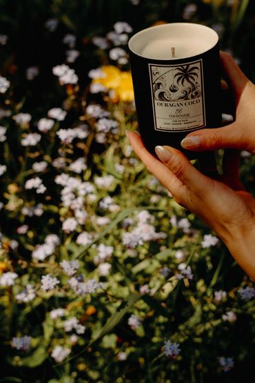Bougie Ouragan Coco 10 oz par Émi Bougie. Des mains qui tiennent la bougie dans un décor naturel.