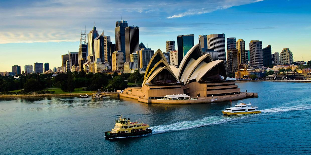 Sydney Opera House with city skyline and boats on water.