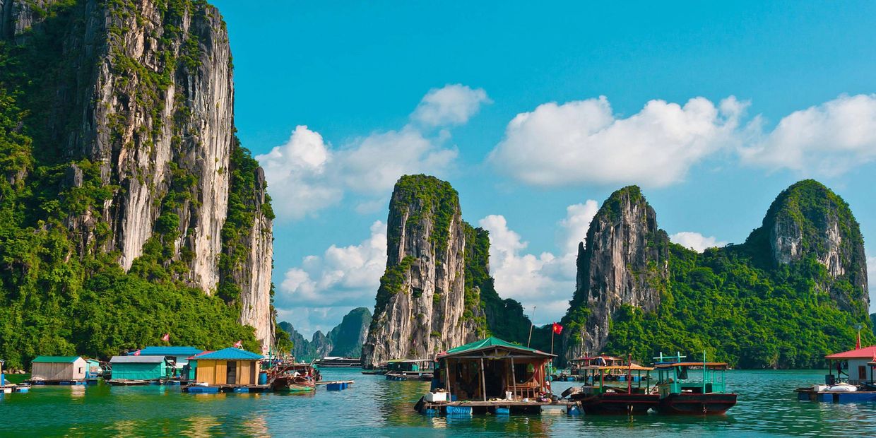 Scenic view of limestone karsts and floating houses on calm water under a bright blue sky.
