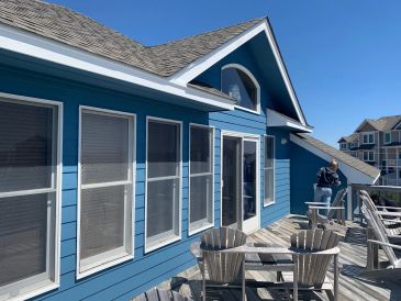 Blue house exterior with wooden deck and chairs under clear sky.