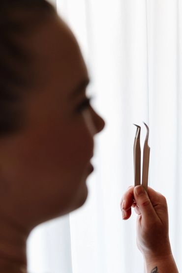 Person holding two precision tweezers with a blurred face background.