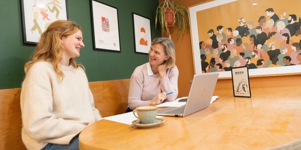 Two women chatting at a table with a laptop and coffee.