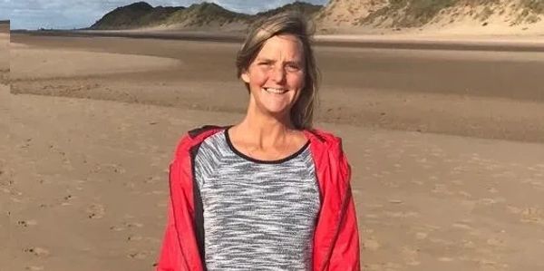 Woman smiling on a sandy beach in a red jacket.
