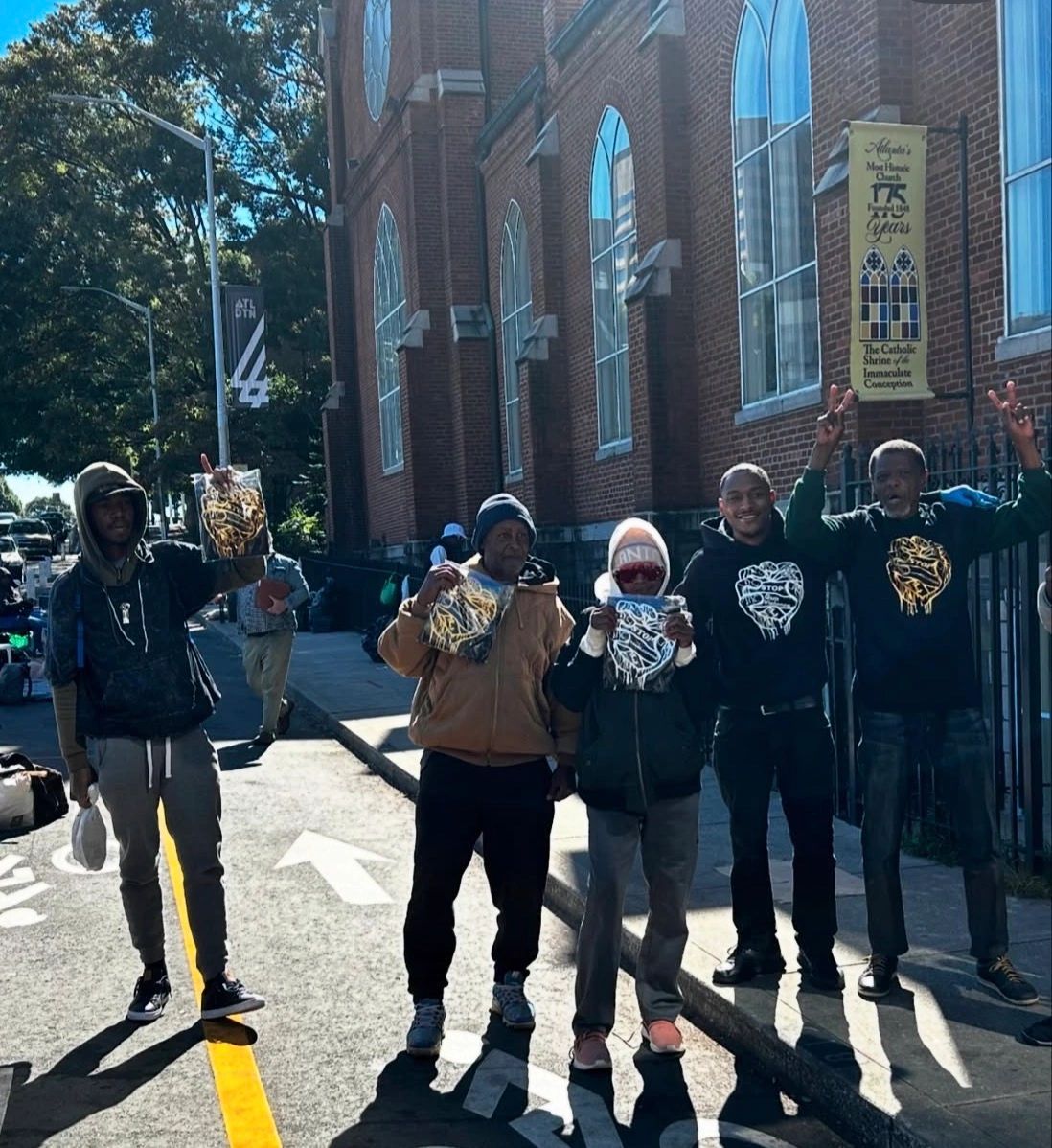 Five people holding up shirts with a raised fist design in front of a church.