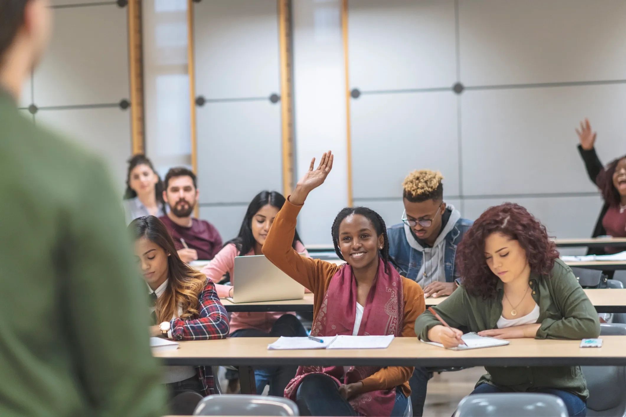 Student raising hand in classroom during lecture.