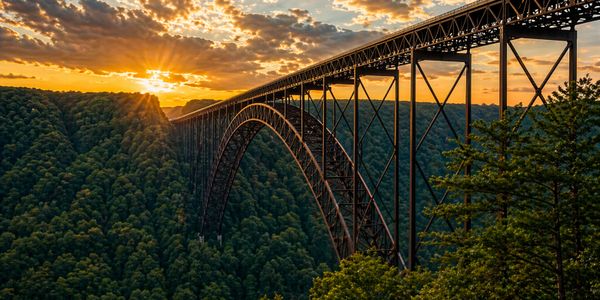 Sunset over a large steel arch bridge spanning a forested valley.