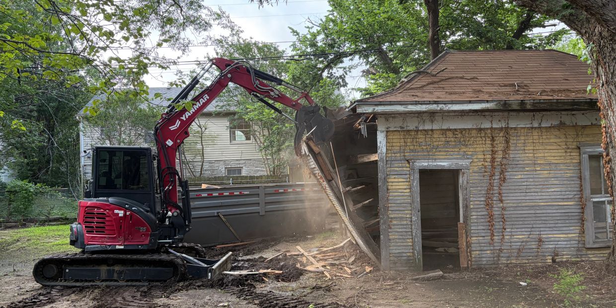 A red excavator demolishing an old wooden house.