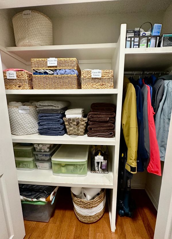 Organized linen and supply closet with labeled baskets and shelves.