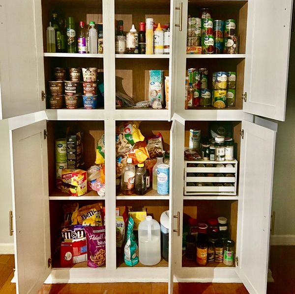 Organized pantry with snacks, canned goods, spices, and condiments in white cabinets.