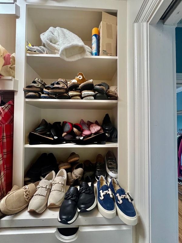 Organized shoe shelves with various shoes and a towel on top.