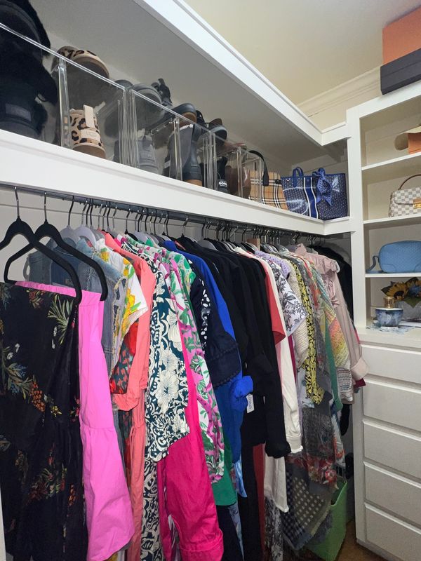 Organized closet with colorful clothes, shoes in clear boxes, and handbags on shelves.