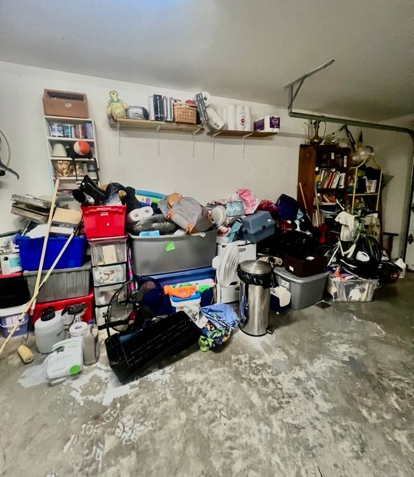Cluttered garage filled with bins, bags, and miscellaneous items.
