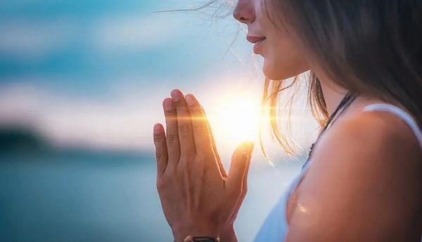 Woman praying with hands together at sunset, peaceful and serene moment.