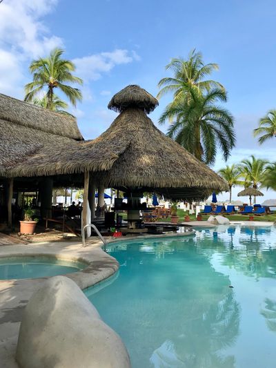 Tropical poolside bar with thatched roof and palm trees.
