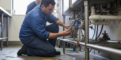Two plumbers fixing pipes under a sink in a utility room.