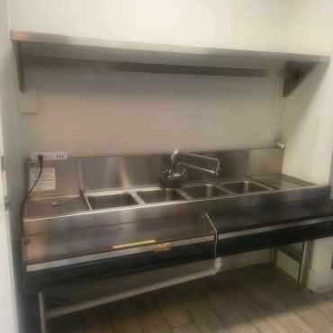 Commercial stainless steel sink with three compartments and a shelf above.