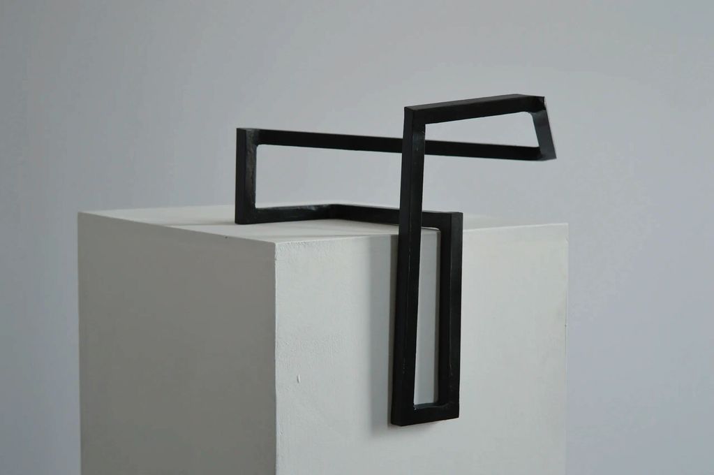 Alternate view of a dark green shape of square steel bars on top & in the middle of a white plinth.