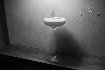 Elegant cocktail with frothy top and leaf garnish in a delicate glass.