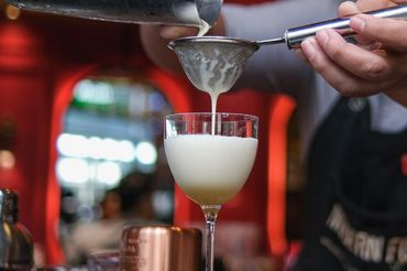 Bartender straining a creamy cocktail into a glass at a bar.