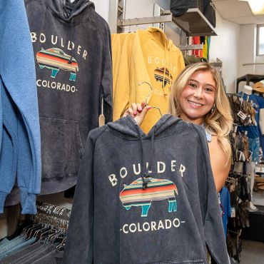 An employee holds up a sweatshirt that says Boulder, Colorado and has a fabric buffalo sewn on