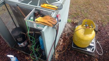 HVAC system being serviced outdoors with tools and refrigerant tank.