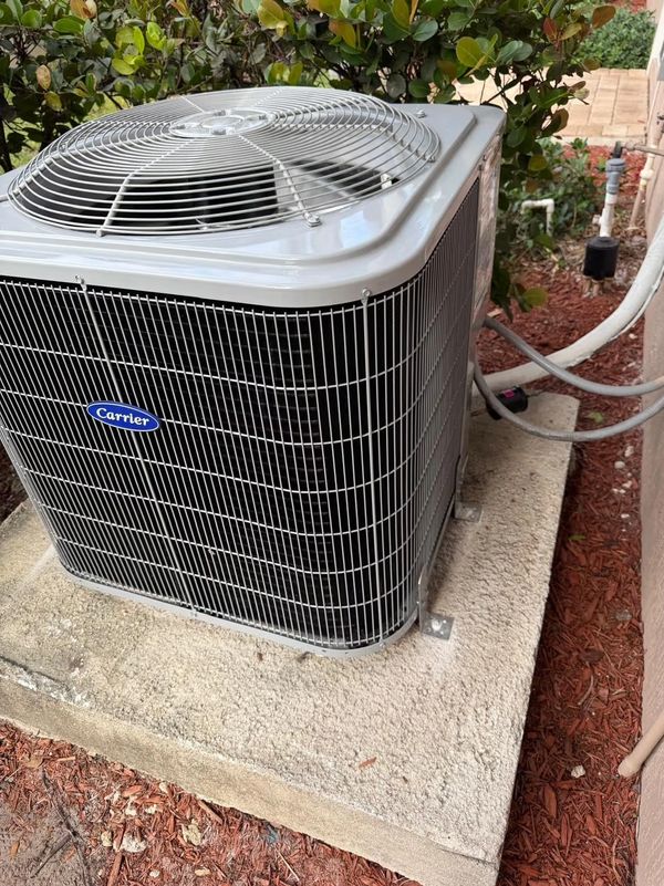 A Carrier brand outdoor air conditioning unit installed on a concrete pad beside a house.