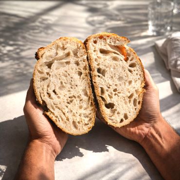 Hands holding a rustic sourdough bread cut in half.