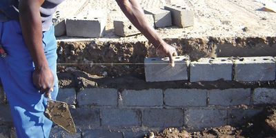A worker laying concrete blocks for a wall foundation.