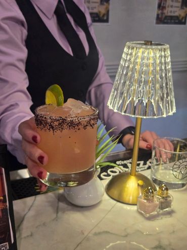 Bartender serving a cocktail with a lime garnish.