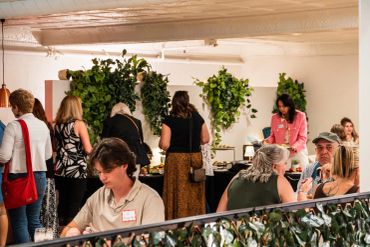 People socializing at an indoor event with greenery.