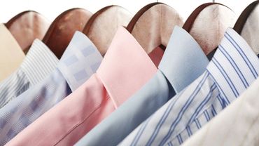 A row of colorful dress shirts neatly hung on wooden hangers.