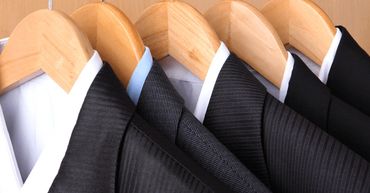Black suits on wooden hangers with white shirts and one blue shirt.