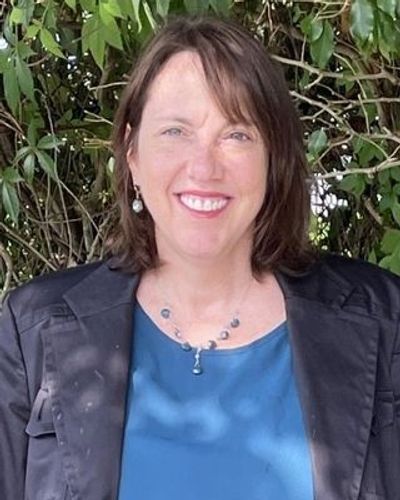 An experienced counselor with brown hair stands in front of green foliage.