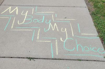 The words "My Body My Choice" written on a sidewalk in yellow and green chalk.