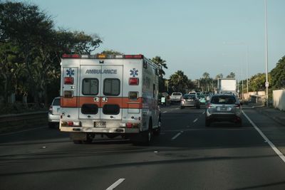 An ambulance, without lights on, driving down a freeway in traffic on a sunny day.