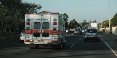An ambulance, without lights on, driving down a freeway in traffic on a sunny day.