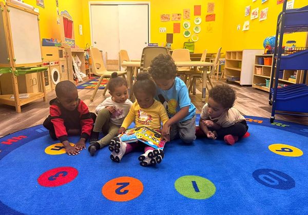 Five young students read together while sitting on a bright blue rug in an Erie, PA classroom.