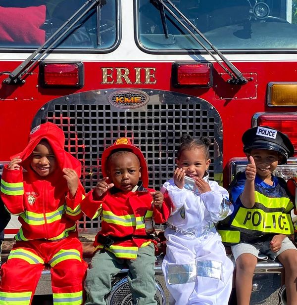 Four young children sitting in front of a red firetruck in Erie, PA.
