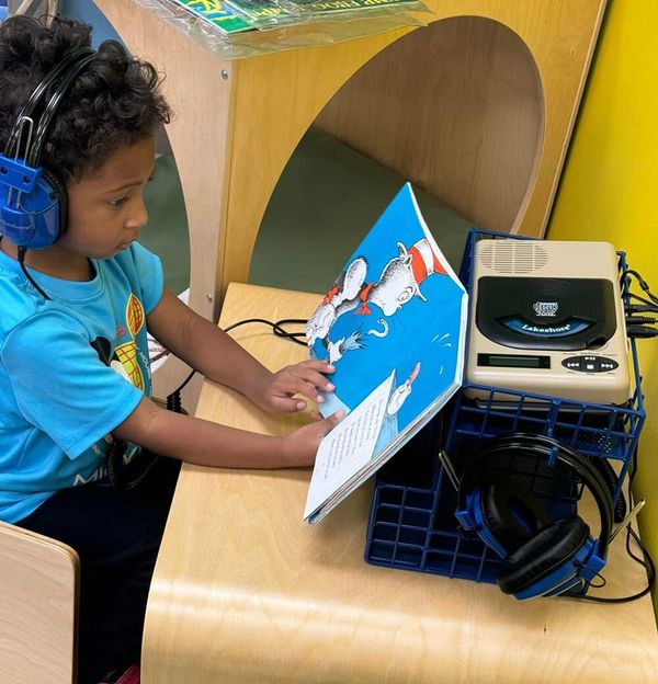 A young student reading "The Cat in the Hat" while wearing headphones.