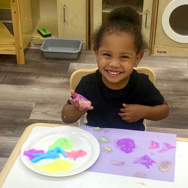 A daycare student at Barb's Childcare Center smiling while finger painting.