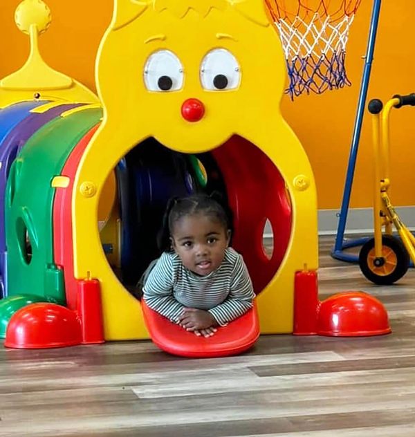 A toddler sits inside a play tunnel that looks like a bright yellow worm.