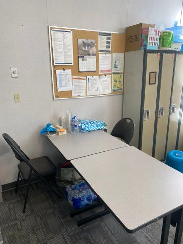 Break room with tables, chairs, water bottles, lockers, and a bulletin board.