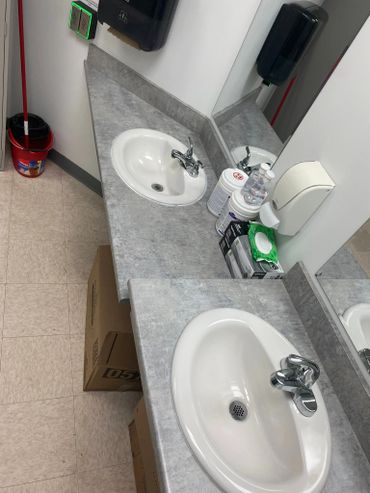Public restroom sink area with cleaning supplies and hand sanitizer.